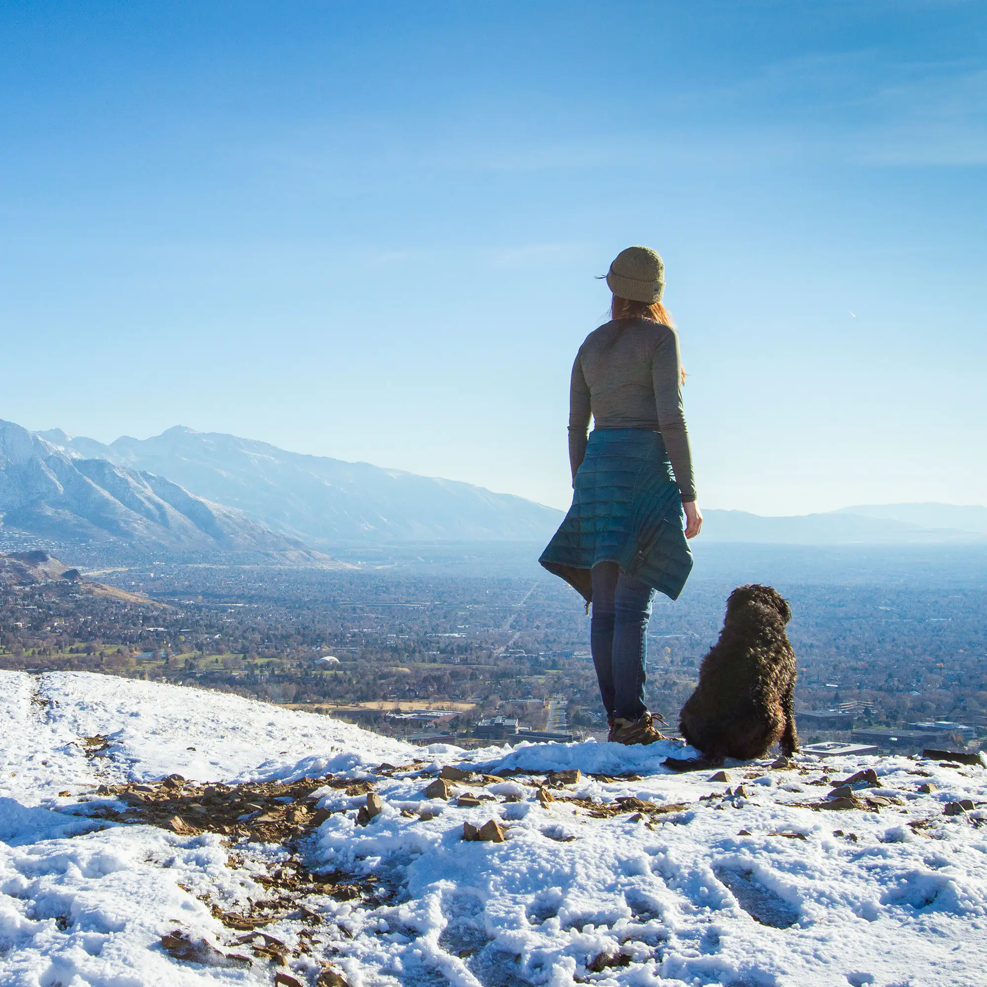 A person and a dog looking at the view on a snowy mountain